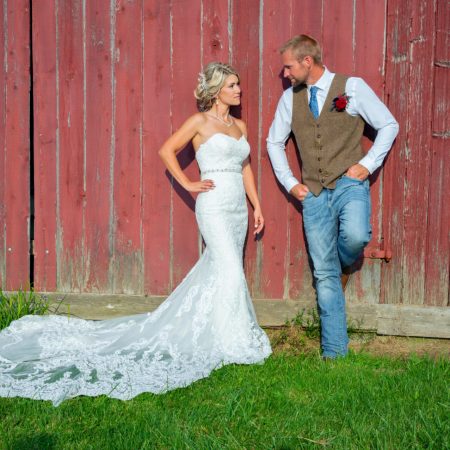 A bride and groom leaning against an old red barn.