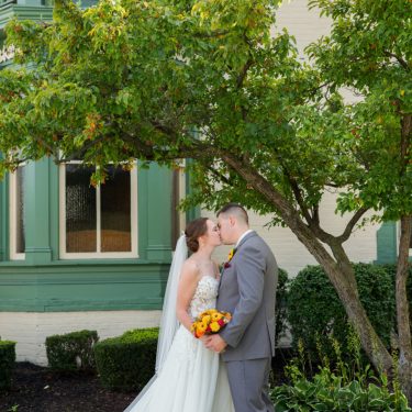 Married couple kissing in front of green house