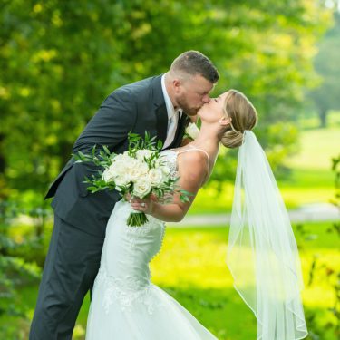 Bride and groom kissing in green field