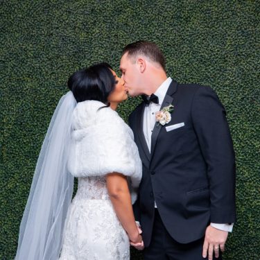 Bride and groom kissing in front of green wall
